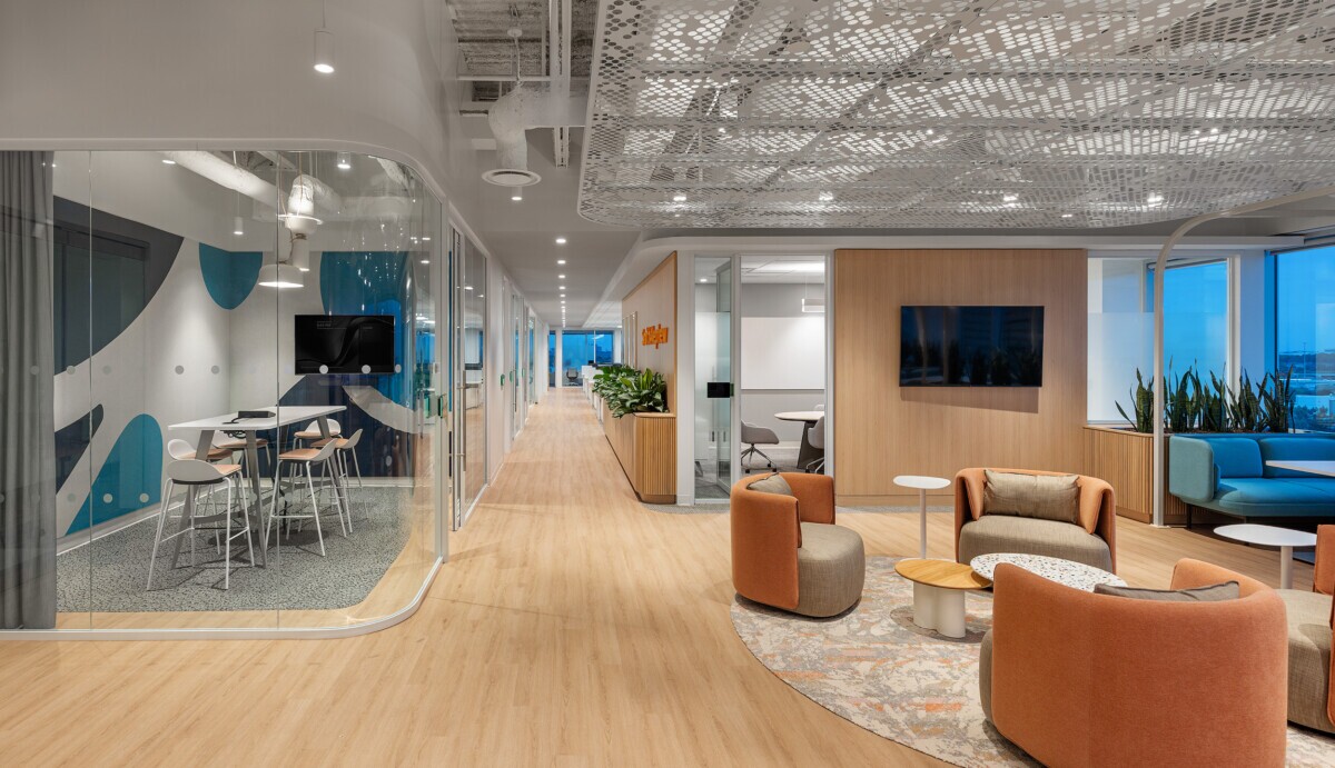 A lounge area and conference room at night in an office space with PANEL:form design perforated ceiling panels at Smith Nephew's office