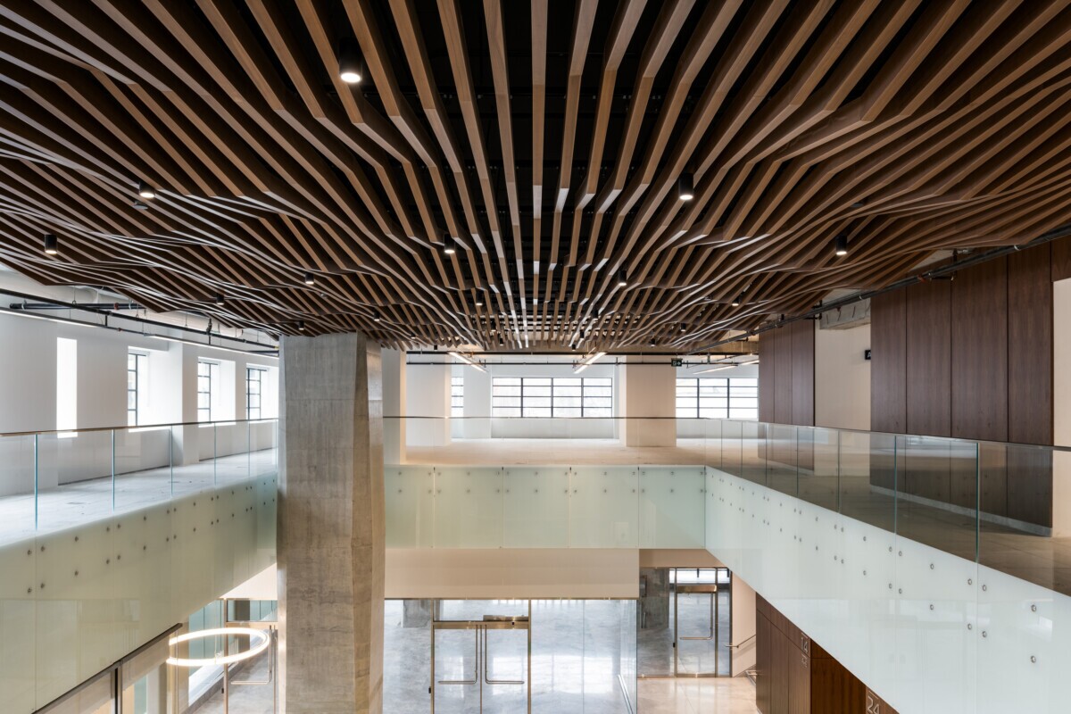 EQ Bank in Toronto, Canada atrium feautring a custom LINE:Form Wave Baffle ceiling feature in extruded metal that flows overhead.The ceiling’s undulating form brings a dynamic sense of movement and architectural expression to the open space. Finished in a warm wood veneer, the baffles offer a material counterpoint to the exposed cement walls, granite flooring, and structural pillars, softening the palette while maintaining a refined, modern aesthetic.
