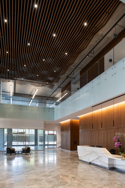 EQ Bank in Toronto, Canada front desk entrance featuring a custom LINE:Form Wave Baffle ceiling feature in extruded metal that flows overhead.The ceiling’s undulating form brings a dynamic sense of movement and architectural expression to the open space. Finished in a warm wood veneer, the baffles offer a material counterpoint to the exposed cement walls, granite flooring, and structural pillars, softening the palette while maintaining a refined, modern aesthetic.