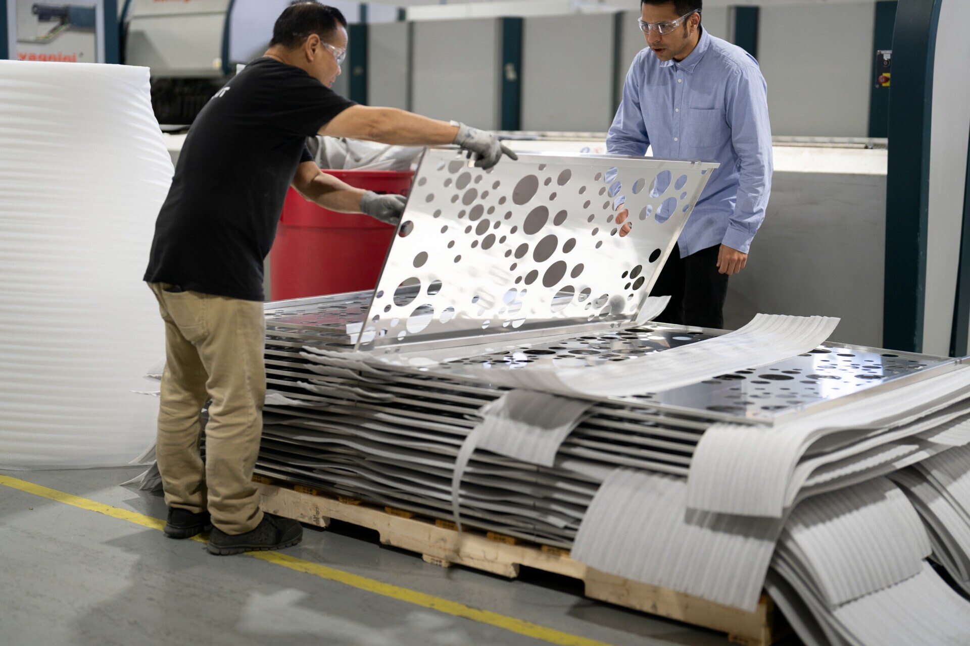 two production staff members inspecting perforated panels